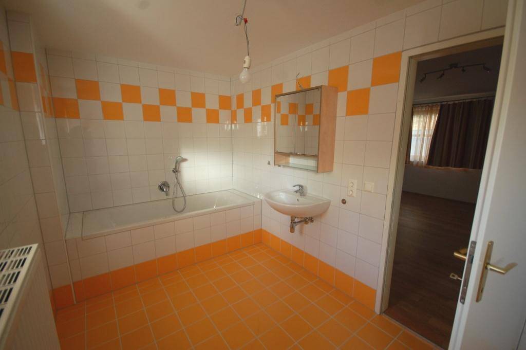 Badezimmer mit orange-weißen Fliesen, Badewanne und Spiegelschrank.