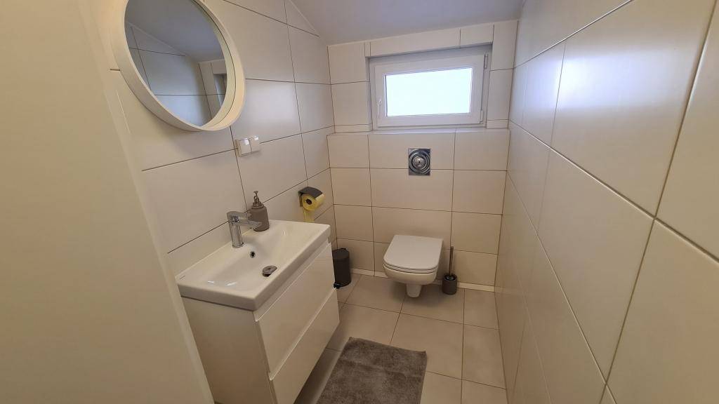 Kleines Gäste-WC mit modernem Waschtisch, Wand-WC und einem Fenster.