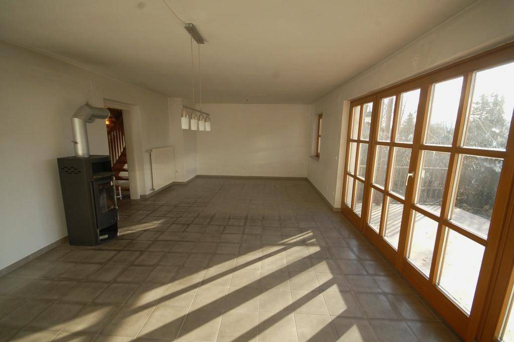 Helles Wohnzimmer mit Fliesenboden, Kaminofen und großen Fenstern zum Garten.