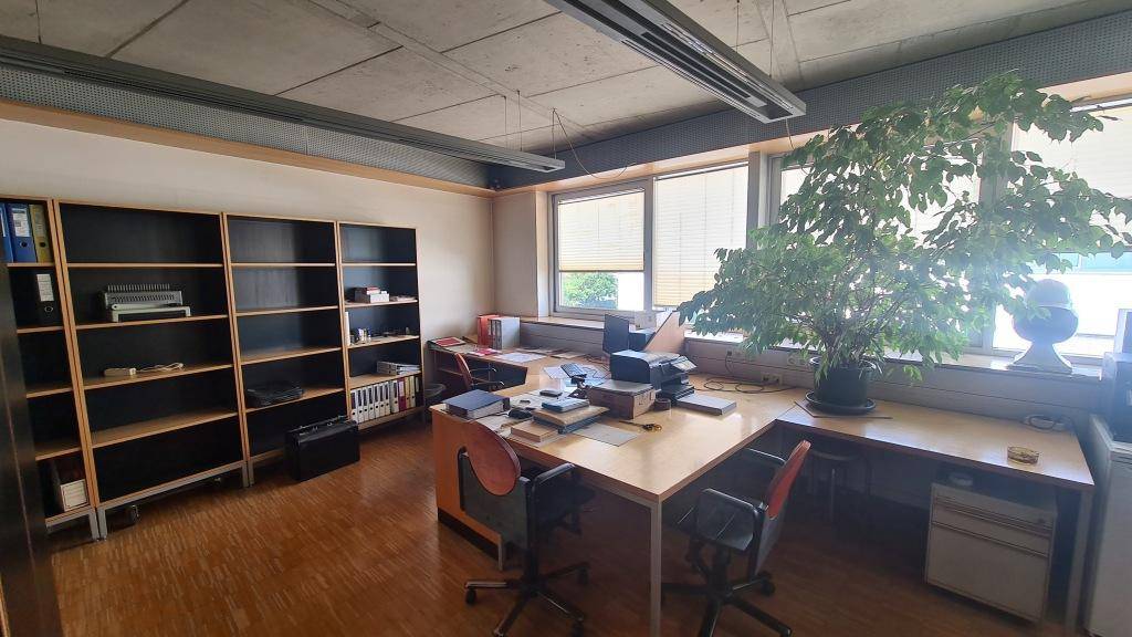 Geräumiges Büro mit mehreren Arbeitsplätzen, Holzparkettboden und großen Fenstern, die eine angenehme Arbeitsatmosphäre schaffen.