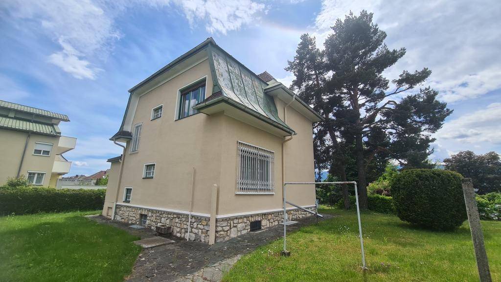Seitenansicht des Hauses mit Mansarddach, beigefarbener Fassade und großem Gartenbereich.