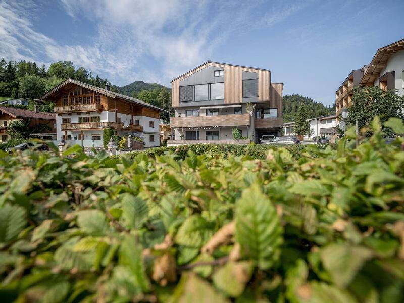 Moderne Architektur mit Holzfassade und großen Fenstern, eingebettet in eine grüne Umgebung mit Bergblick.