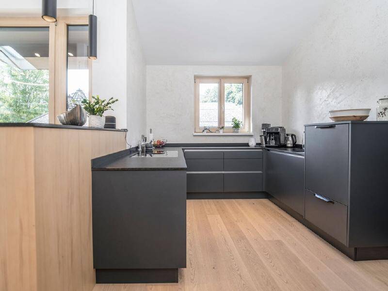 Moderne Küche mit dunklen Schränken, Holzakzenten und einem Fenster für Tageslicht.