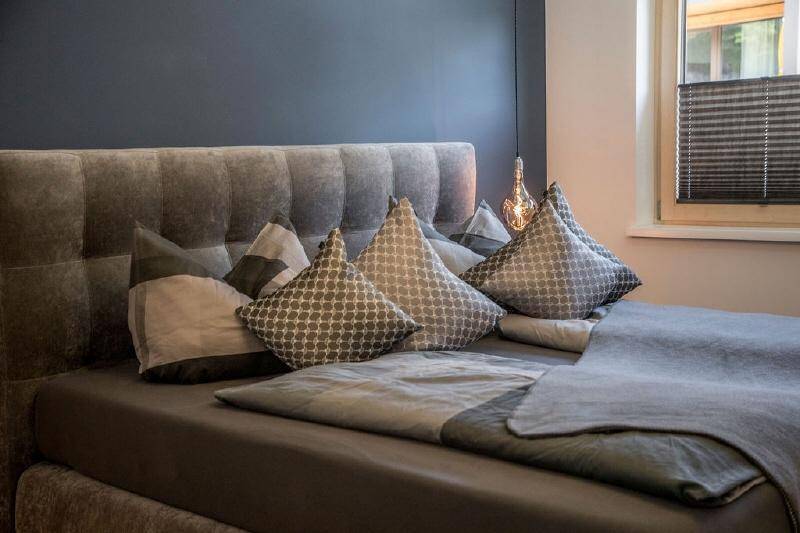 Gemütliches Schlafzimmer mit großem Polsterbett, dunkler Akzentwand und Fenster.