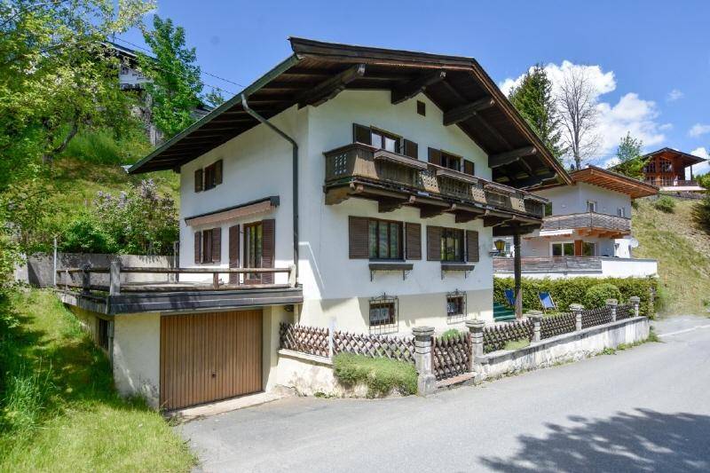 Charmantes Alpenhaus mit traditioneller Architektur, Holzbalkonen und Garage an einer ruhigen Straße.