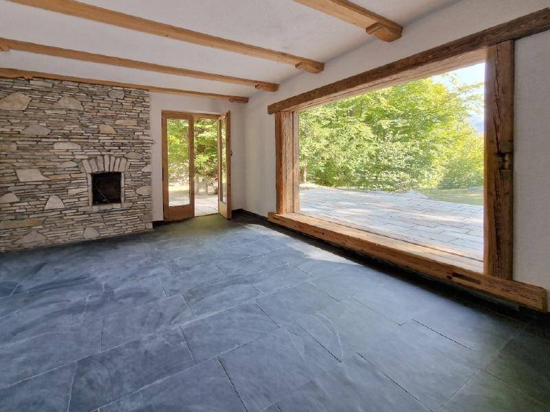 Geräumiger Innenraum mit Steinwand, Holzbalken und großem Fenster mit Blick ins Grüne.