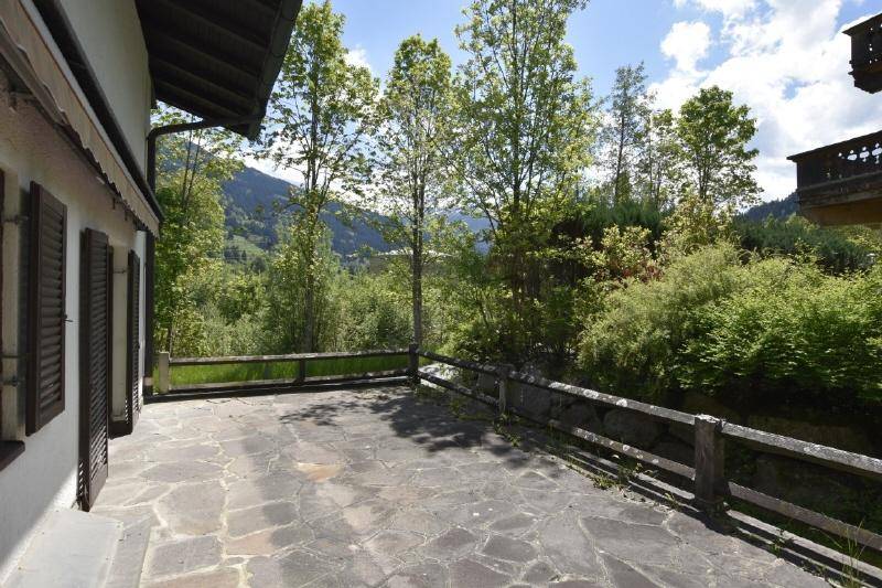 Geräumige Steinterrasse mit Holzzaun und weitem Blick auf die grüne Berglandschaft.