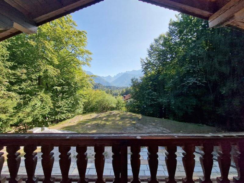 Blick vom Balkon auf die umliegende Berglandschaft und grüne Wälder unter blauem Himmel.