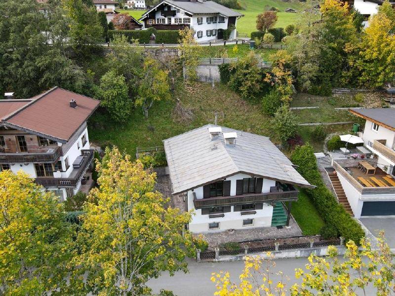 Luftaufnahme des Anwesens mit Satteldach und umliegenden Häusern in einer grünen Hügellandschaft.