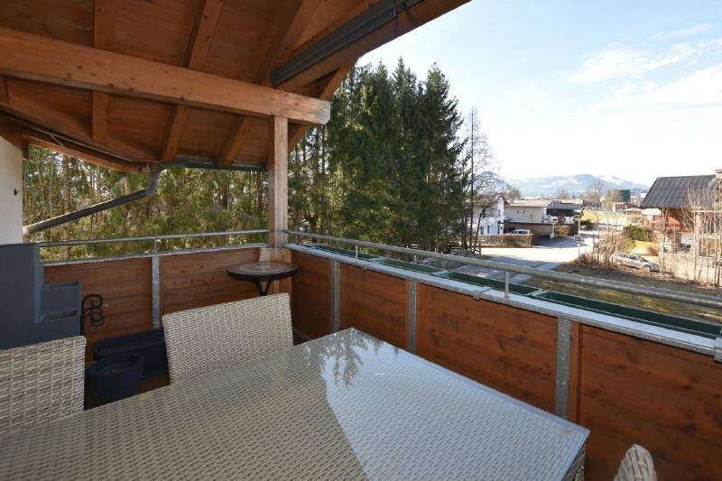 Sonniger Balkon mit Holzboden, Sitzgelegenheiten und Blick auf die umliegende Landschaft.