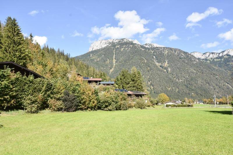 Idyllische Landschaft mit grünen Wiesen, Häusern am Hang und imposanten Bergen im Hintergrund.