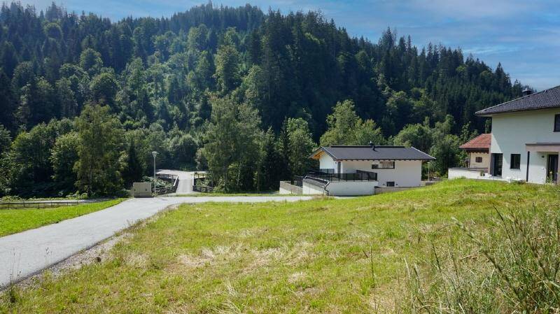 Moderne Wohnanlage mit Zufahrtsweg, umgeben von weitläufigen Grünflächen und Wald mit Bergblick.