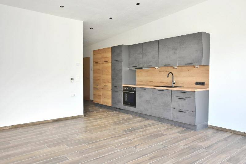 Funktionale L-förmige Küchenzeile mit grauen Fronten und Holzdetails in einem lichtdurchfluteten Raum.