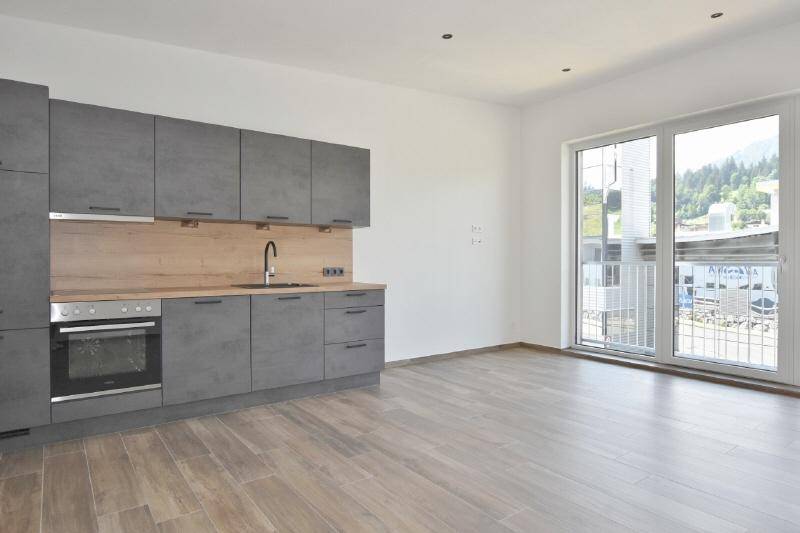 Moderne Küchenzeile in Grau mit Holzakzenten und Zugang zu einem Balkon in einem hellen Raum.
