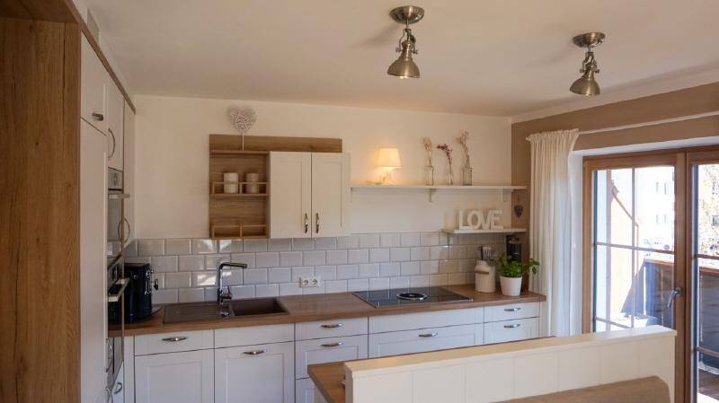 Helle Einbauküche mit weißen Schränken, Holztheke und Zugang zum Außenbereich.