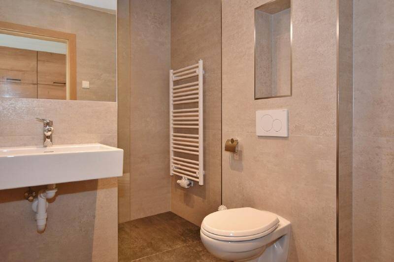 Modernes Badezimmer mit beigefarbenen Fliesen, wandhängendem WC und einem beheizten Handtuchhalter.