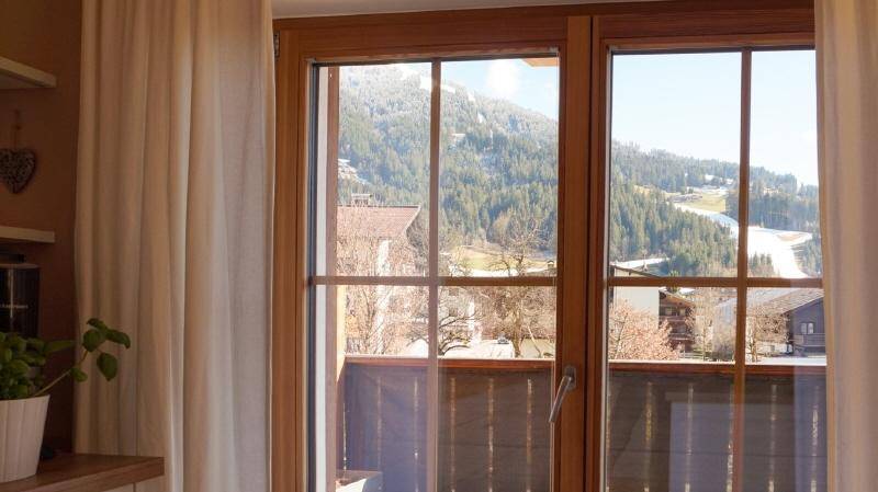Fenster mit malerischem Blick auf schneebedeckte Berge und eine Skipiste.