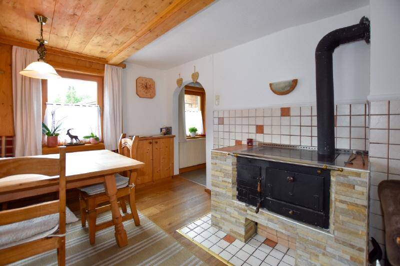 Rustikaler Essbereich mit traditionellem Holzofen und Holzbalkendecke, typisch für alpines Wohnen. 