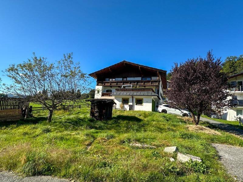 Traditionelles Haus mit Holzbalkonen und Satteldach, umgeben von grünen Wiesen und Bäumen an einem sonnigen Tag.