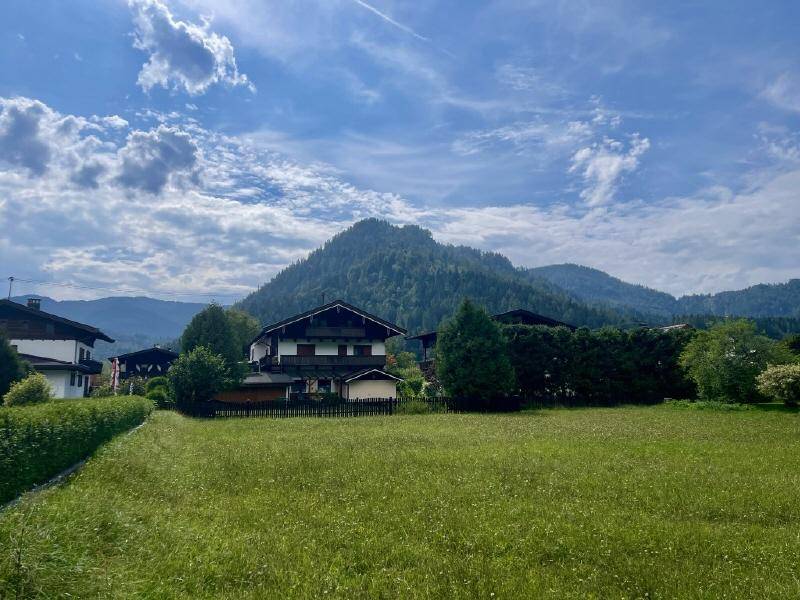 Grünes Feld mit einem charmanten Haus im traditionellen Stil, umgeben von Bäumen und Hecken.