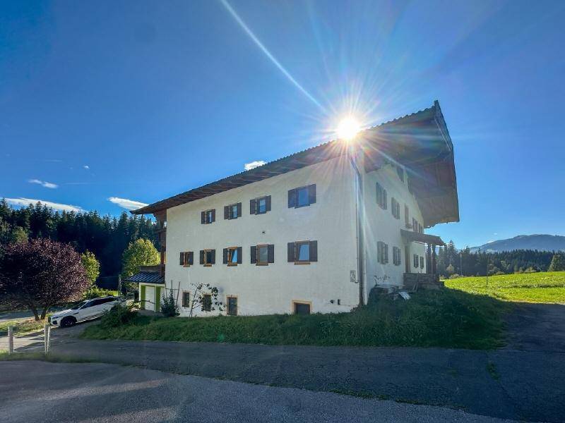 Traditionelles Haus mit weißer Fassade und braunen Fensterläden unter strahlend blauem Himmel und Sonnenschein.