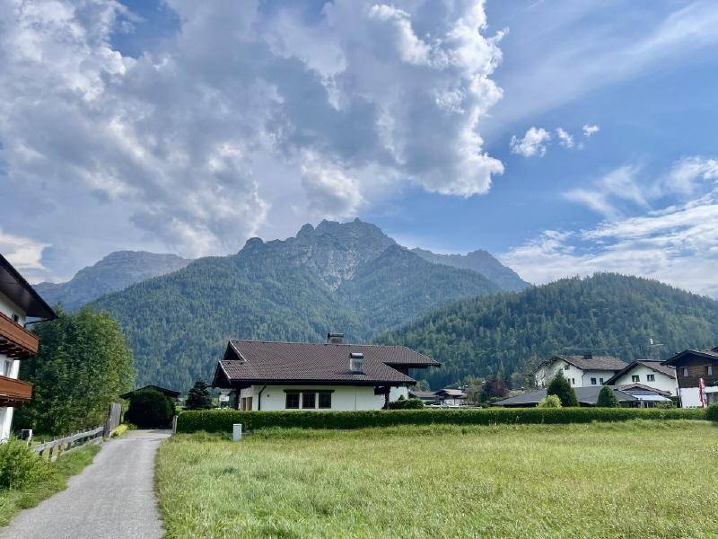 Charmantes Haus mit gepflegter Hecke und Zufahrtsweg, umgeben von einer malerischen Berglandschaft.