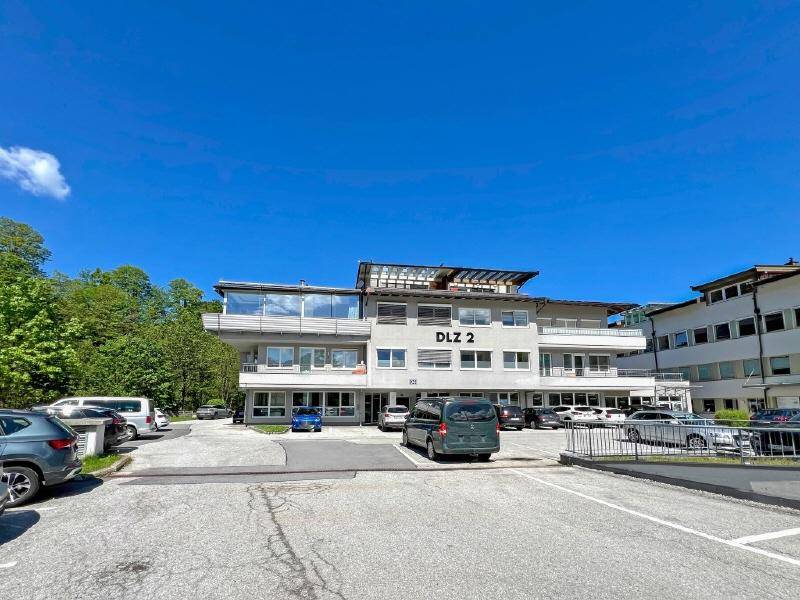 Modernes Geschäftsgebäude mit großem Parkplatz und vielen Fenstern unter blauem Himmel.