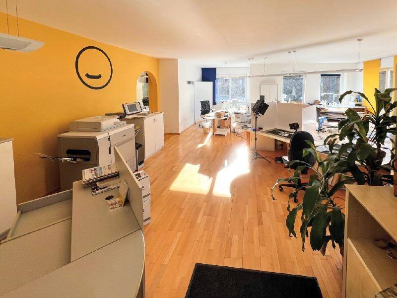 Helles, offenes Büro mit gelber Akzentwand, Holzboden und viel Tageslicht.