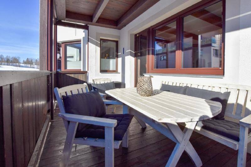 Überdachter Balkon mit Holzboden, Sitzgelegenheiten und weitem Blick auf die winterliche Landschaft.