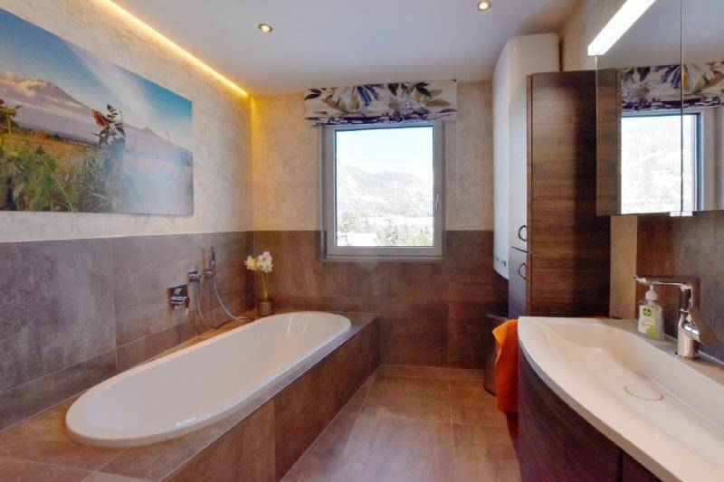 Modernes Badezimmer mit Badewanne, Fenster und Blick auf die verschneite Berglandschaft.