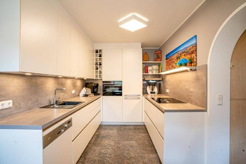Moderne Einbauküche mit weißen Fronten, integrierten Geräten und minimalistischem Design.