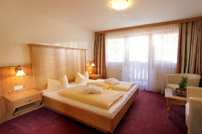 Helles Schlafzimmer mit Doppelbett, Holzmöbeln, rotem Teppich und einem großen Fenster mit Vorhängen.