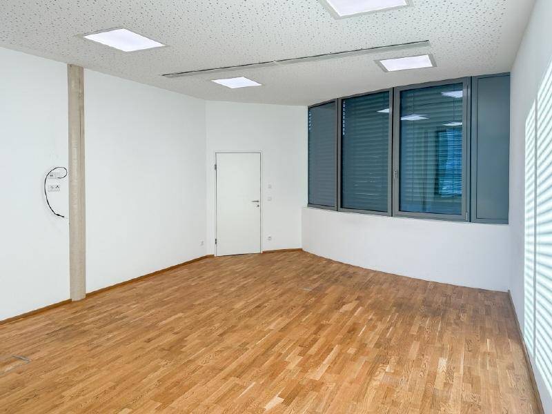 Moderner Büroraum mit großen Fenstern, Jalousien und hochwertigem Holzboden.
