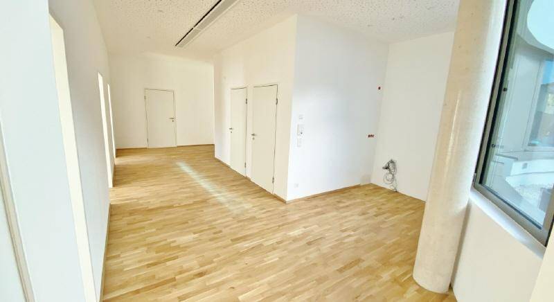 Geräumiger Büroraum mit hellem Holzboden, hohen Decken und moderner Ausstattung.