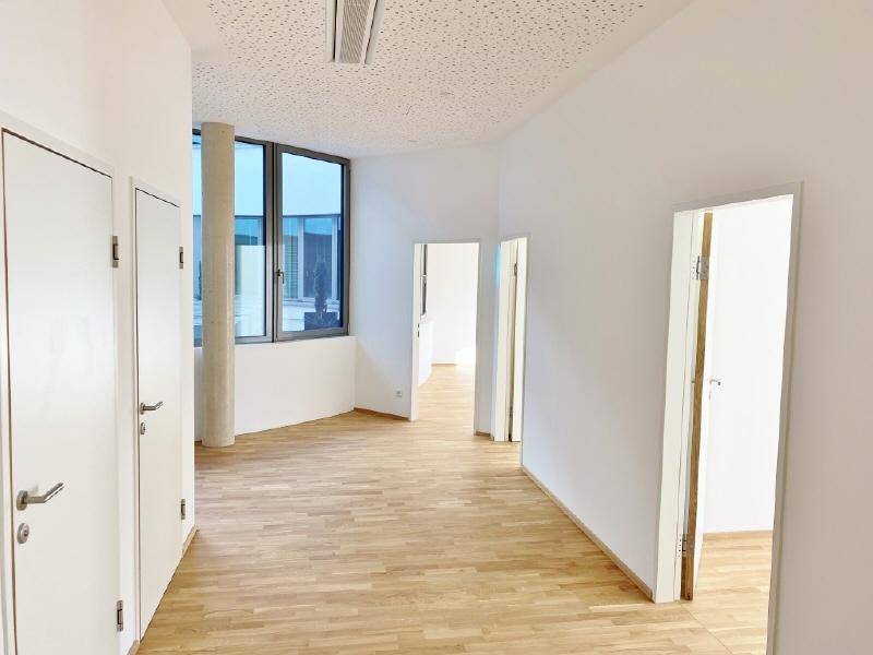 Heller Büroraum in einem Neubau mit großen Fenstern und Holzboden.