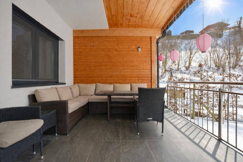 Überdachter Balkon mit gemütlicher Sitzgruppe und Blick auf die verschneite Landschaft.