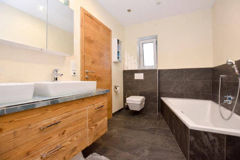 Modernes Badezimmer mit Doppelwaschbecken, Badewanne und dunklen Fliesen.