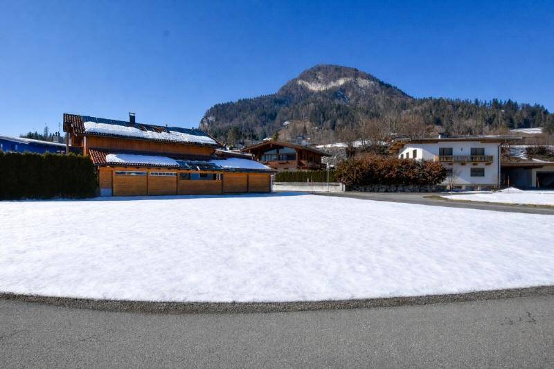 Helles Grundstück mit schneebedeckter Fläche, umgeben von Hecken und einem majestätischen Bergblick.