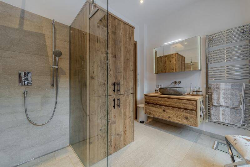 Modernes Badezimmer mit begehbarer Dusche, Natursteinwaschbecken und Holzmöbeln.
