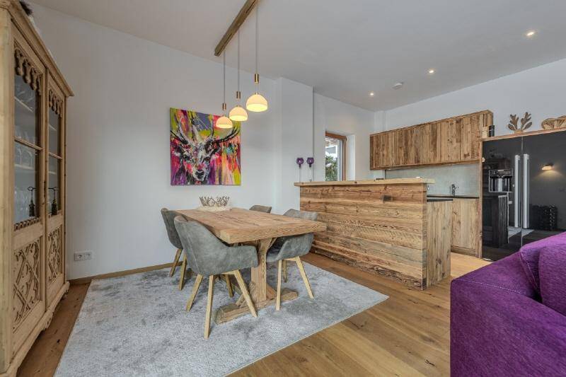 Essbereich mit rustikalem Holztisch und moderner Kunst, angrenzend an die offene Holzküche.