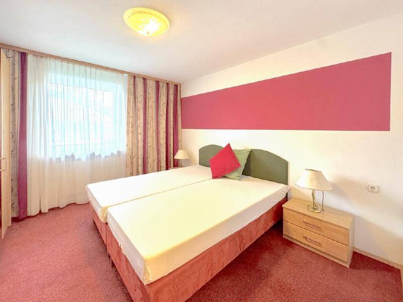 Schlichtes Schlafzimmer mit zwei Einzelbetten, rotem Teppichboden und farbiger Wandgestaltung.