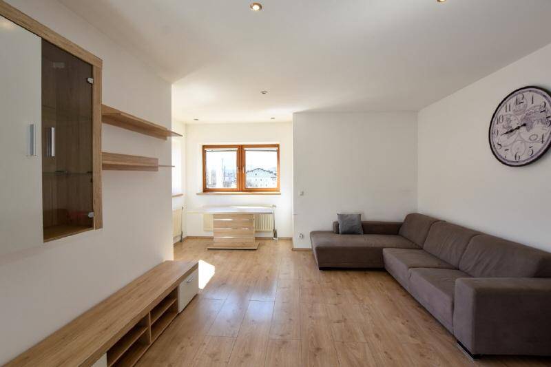 Geräumiges Wohnzimmer mit großem Ecksofa, Holzboden und Fenster mit Blick nach draußen.