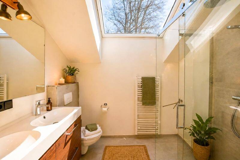 Modernes Badezimmer mit großer Dusche, Doppelwaschbecken und viel Tageslicht durch das Dachfenster.