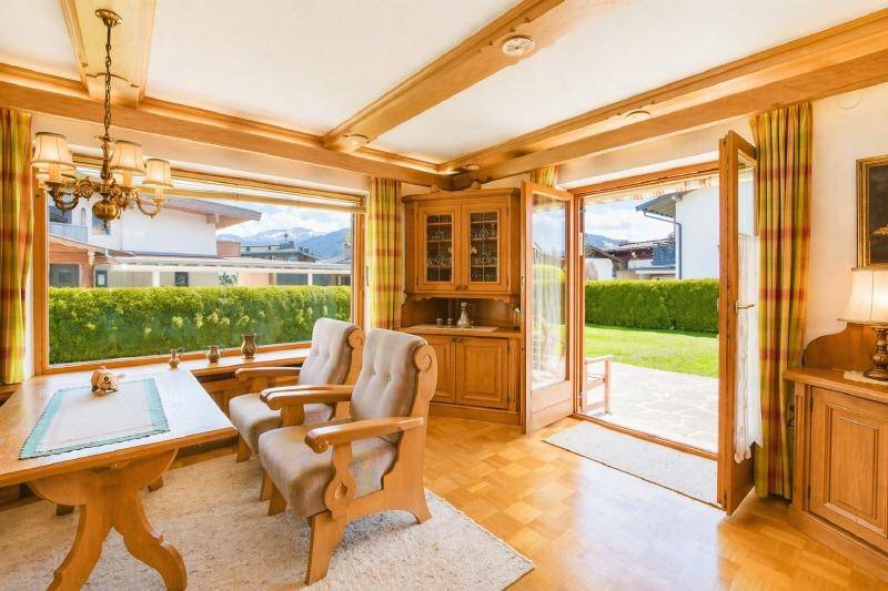 Heller Wohnbereich mit Holzmöbeln, großen Fenstern, Zugang zum Garten und Bergblick.