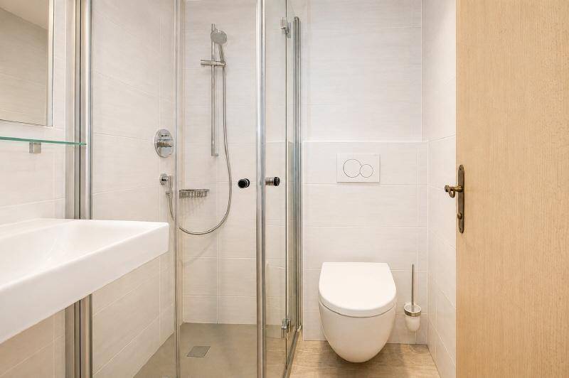 Modernes Badezimmer mit ebenerdiger Dusche, wandhängendem WC und Einzelwaschbecken in hellen Fliesen.
