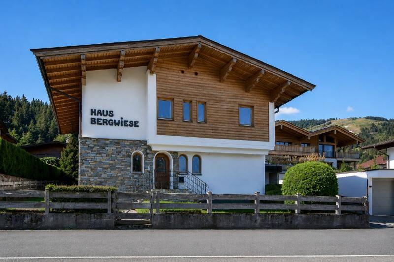 Die Vorderseite des Hauses "Haus Bergwiese" mit Steinfassade und Holzelementen, umgeben von alpiner Natur.