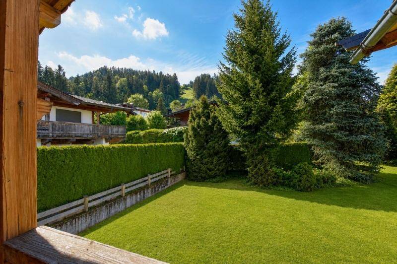 Gepflegter Rasenbereich mit hoher Hecke und Bäumen, gesehen von einem Balkon oder einer Terrasse.