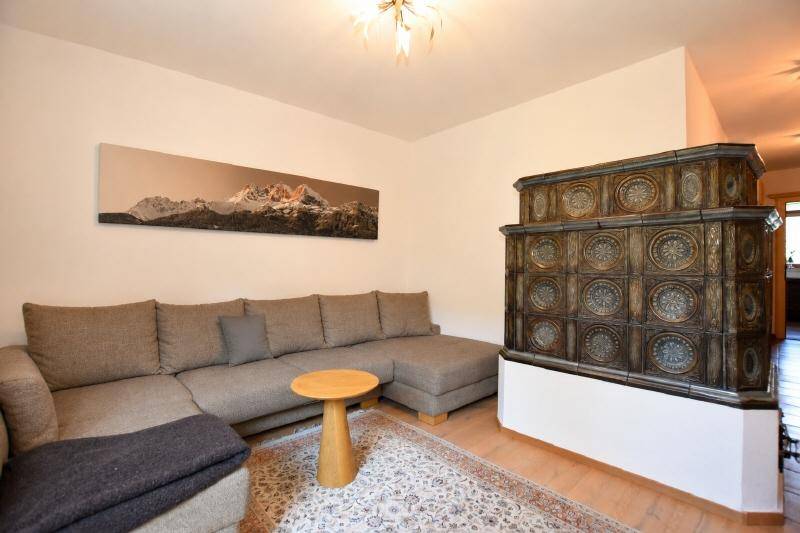 Gemütliches Wohnzimmer mit großem Sofa, traditionellem Kachelofen und Holzboden, ideal zum Entspannen.