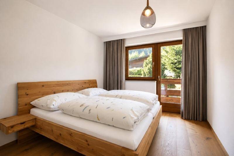 Helles Schlafzimmer mit Doppelbett aus Holz, Nachttischen und Zugang zu einem Balkon oder einer Terrasse.