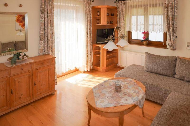Sonniges Wohnzimmer mit Holzboden, bequemer Couch und Zugang zum Balkon.